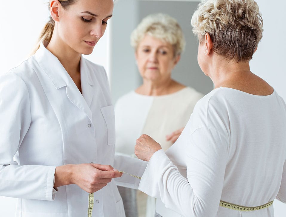 Pielęgniarka mierząca BMI i wymiary starszej pani